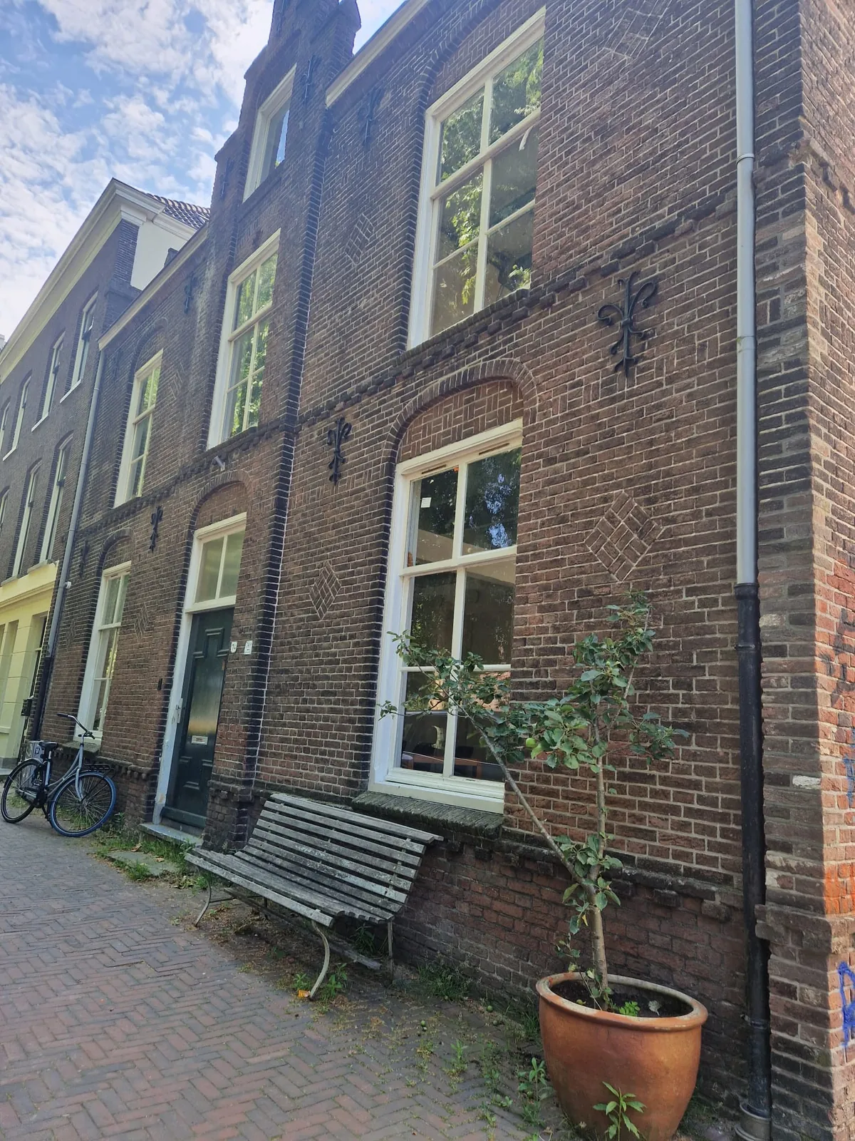 Brick facade of Maliesingel 74 with fleur-de-lis wrought-iron wall anchors and a bench by the door