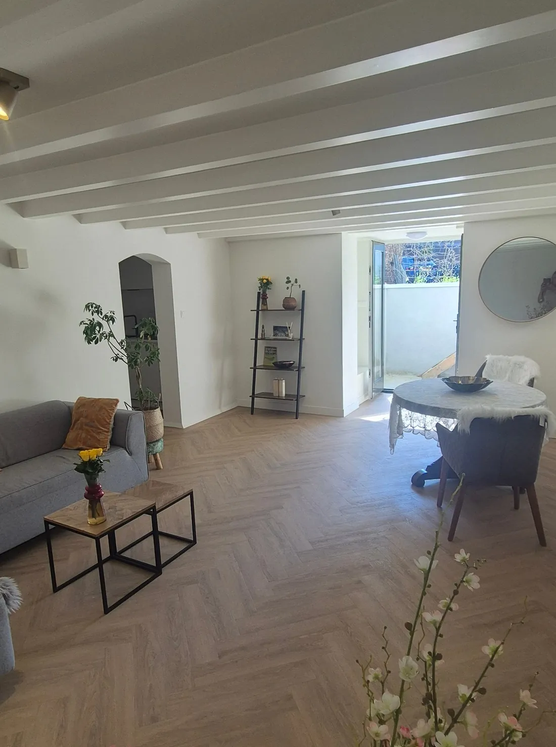 Bright living room with white beams, herringbone floor, sofa and dining table by the garden door